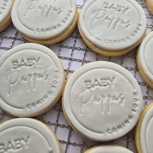 multiple of the same circular cookie with olive coloured icing coating a sugary shortbread. The icing is imprinted with the words Baby Coming Soon.